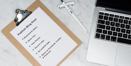 A photo with a laptop and a sheet of paper with the written down steps on how to publish a blog post